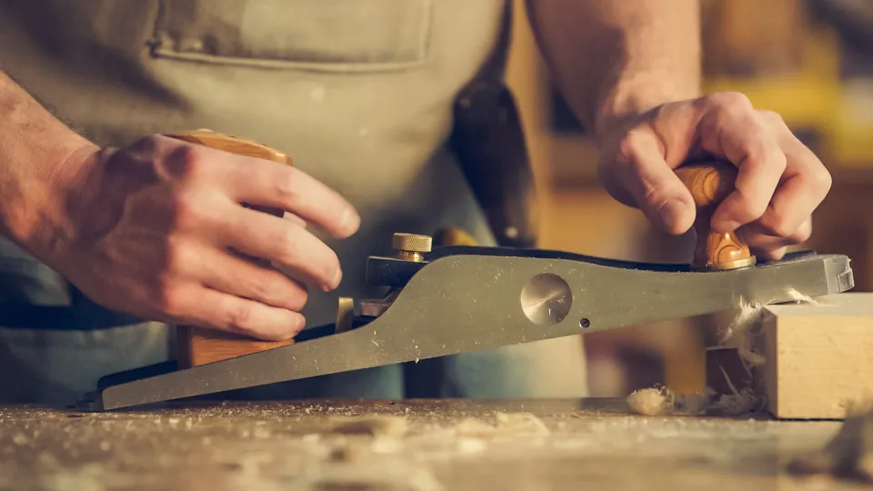 Mains d'un artisan menuisier rabotant une planche